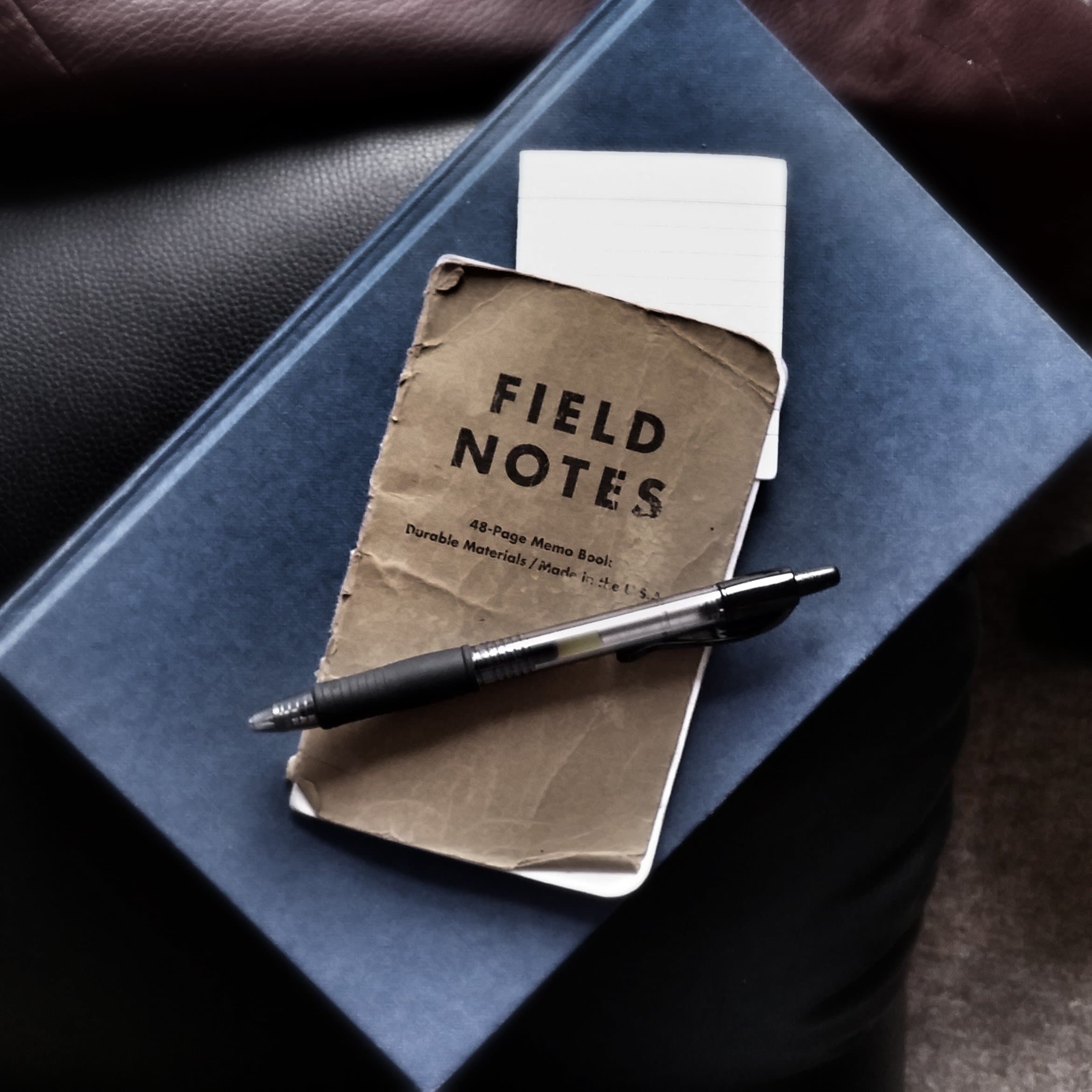 A well-used Field Notes notebook and pen on a blue book.