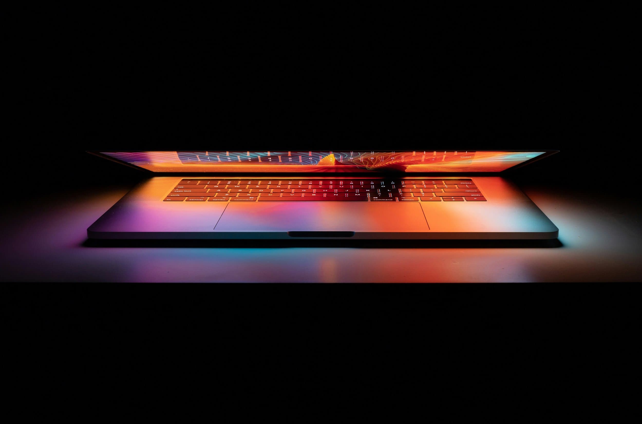 A partly open laptop illuminated by colourful light against a dark background.